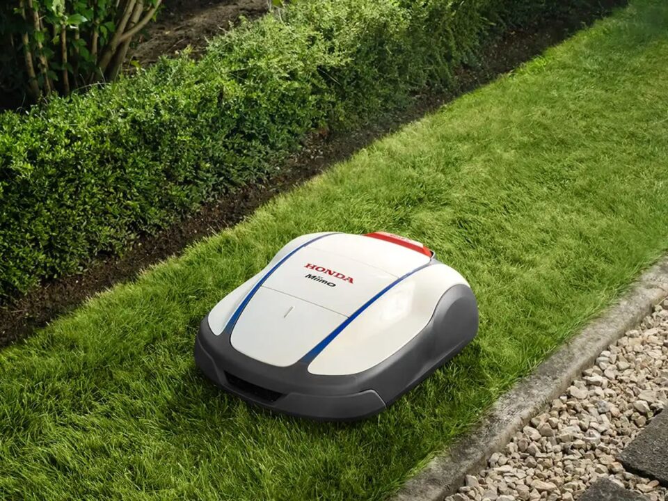 A robotic lawn mower on neatly trimmed grass beside hedges.